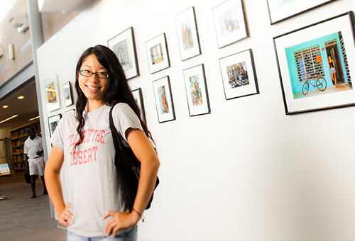 Photo of a student in front of a white wall with photos on it.